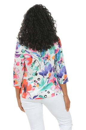 Woman wearing a colorful floral blouse with white pants on a white background. Back shot.