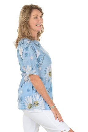 A woman wearing a blue short sleeve shirt with a daisy pattern. Side shot.