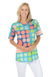 A woman wearing a green multi short sleeve shirt with a multi colored dot pattern.
