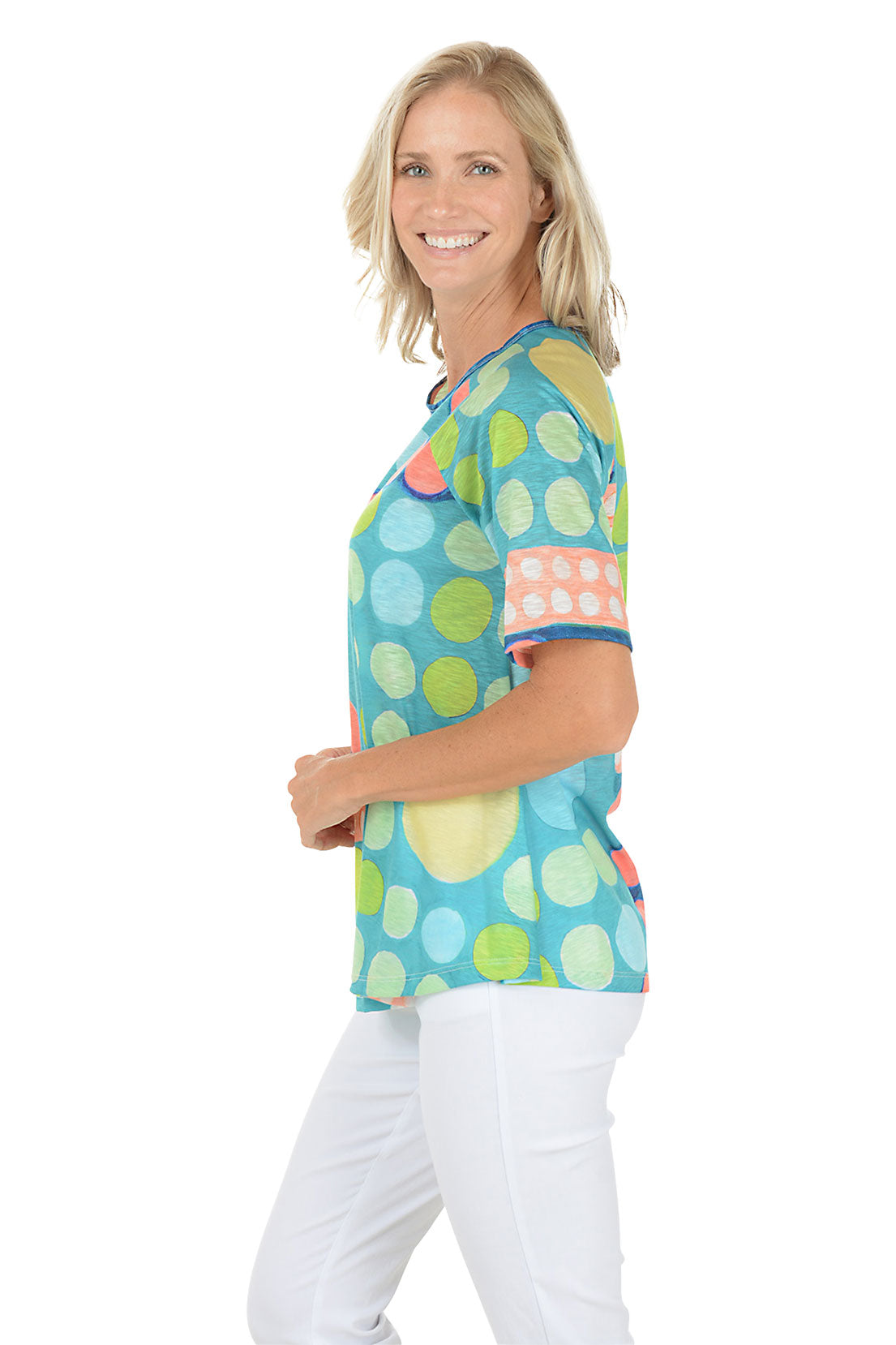 A woman wearing a green multi short sleeve shirt with a multi colored dot pattern. Side shot.