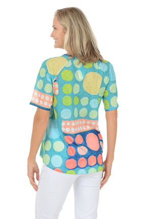 A woman wearing a green multi short sleeve shirt with a multi colored dot pattern. Back shot.