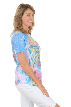 A woman wearing a blue short sleeve top with an abstract floral pattern. Side shot.