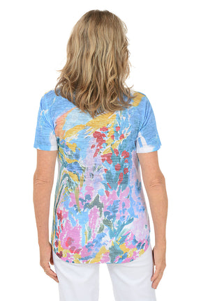 A woman wearing a blue short sleeve top with an abstract floral pattern. Back shot.