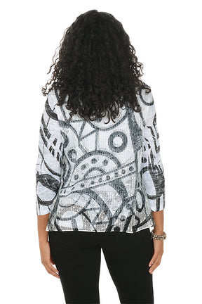Woman wearing a patterned top and black pants on a white background. Back shot.