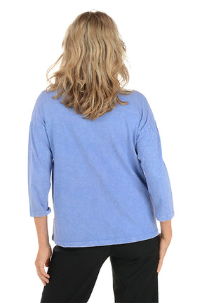 A woman wearing a 3/4 sleeve blue top with a palm tree pattern detail. Back shot.