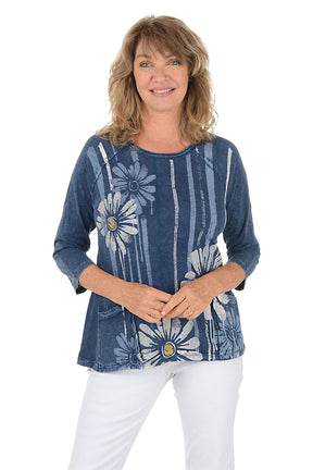 A woman wearing a blue 3/4 sleeve shirt with a daisy pattern.