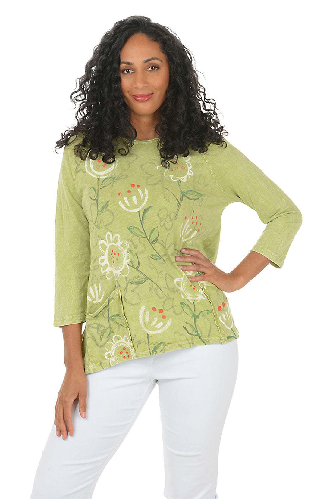 Woman wearing a green floral blouse with white pants on a white background.