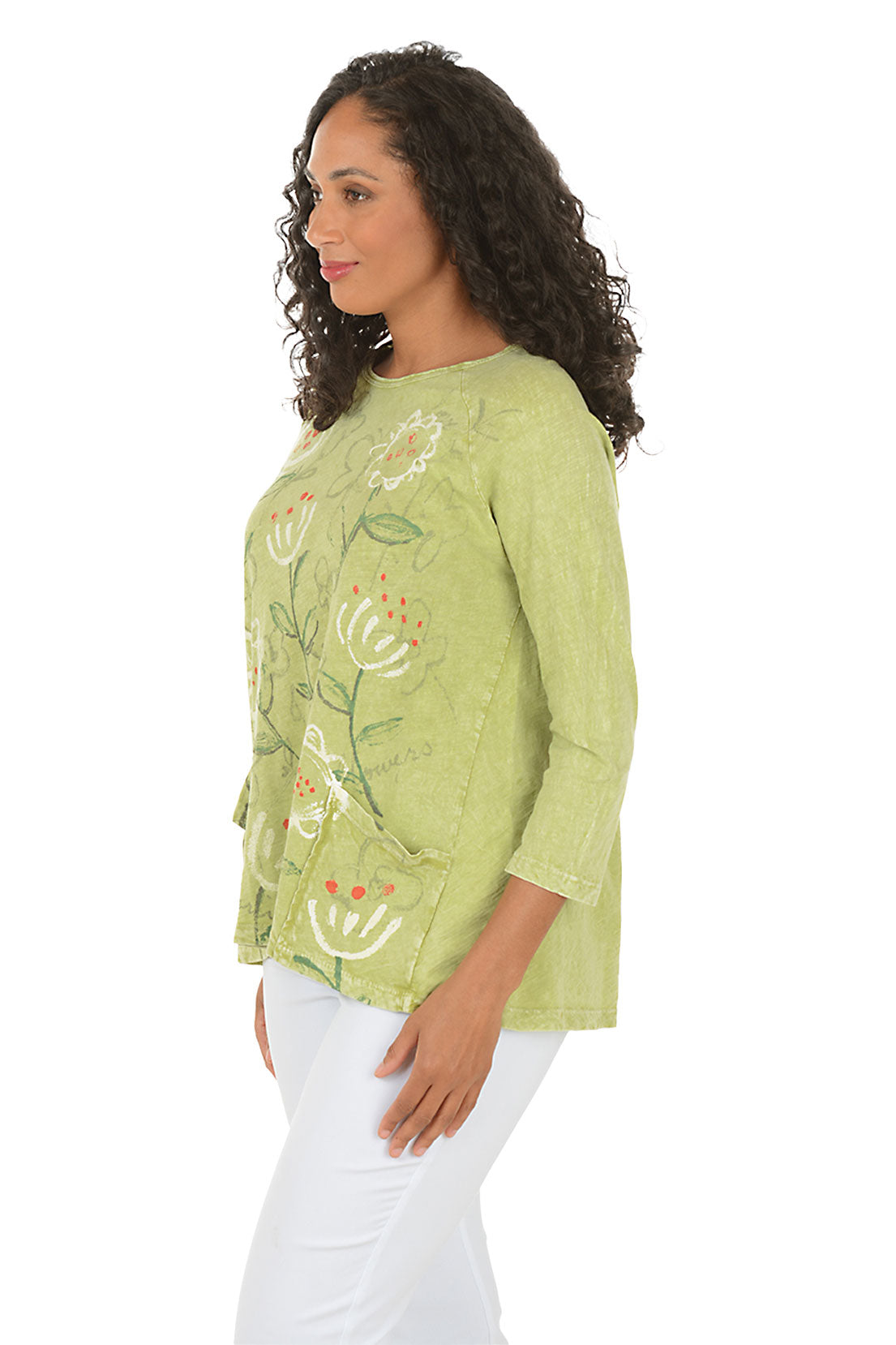 Woman wearing a green floral blouse with white pants on a white background. Side shot.