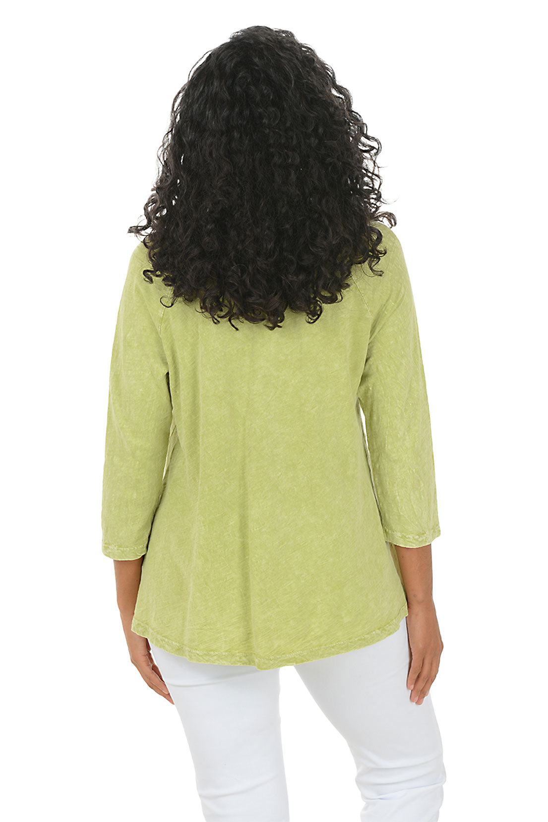 Woman wearing a green floral blouse with white pants on a white background. Back shot.