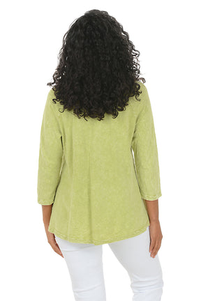 Woman wearing a green floral blouse with white pants on a white background. Back shot.