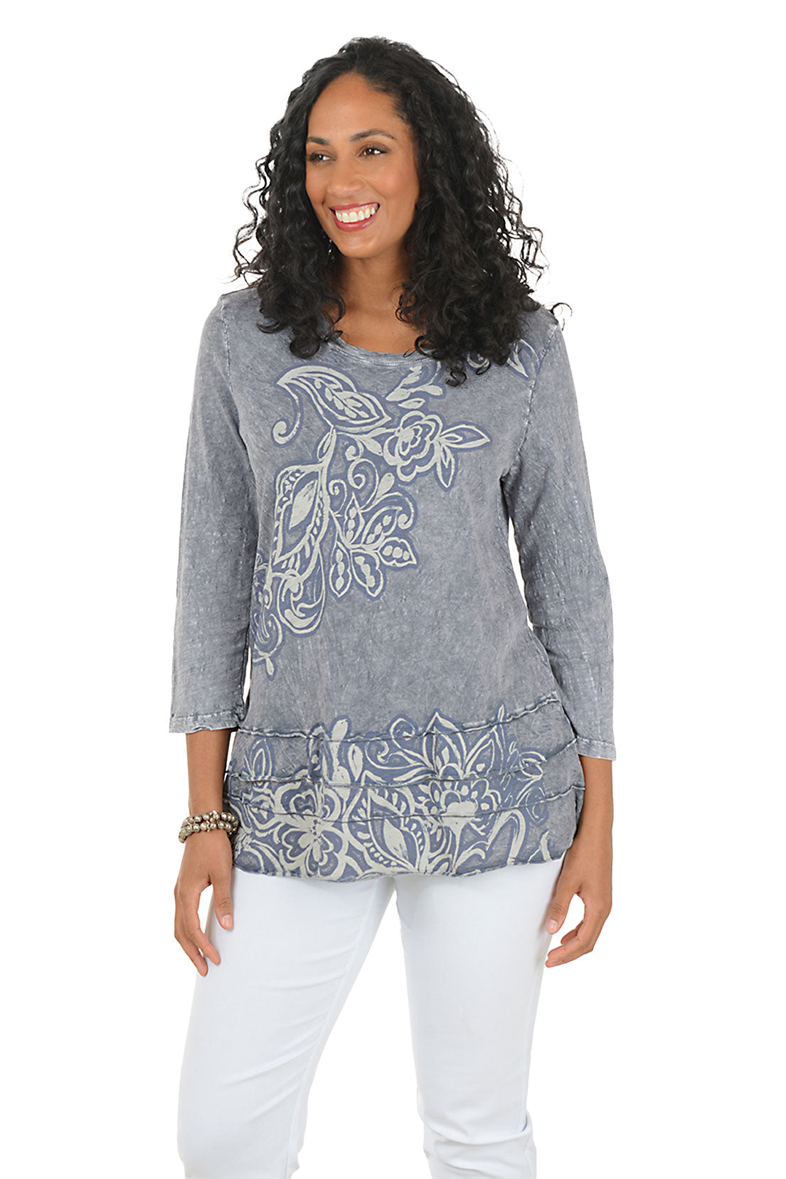 Woman wearing a gray floral-patterned top and white pants on a white background.