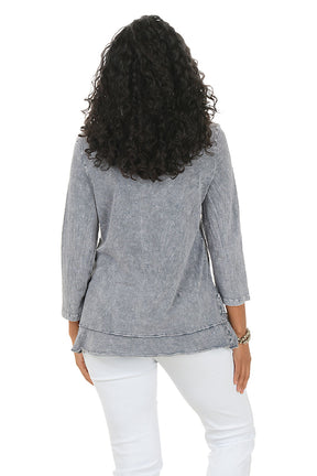 Woman wearing a gray floral-patterned top and white pants on a white background. Back shot.