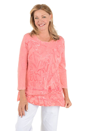 Woman wearing a pink floral blouse with white pants on a white background.