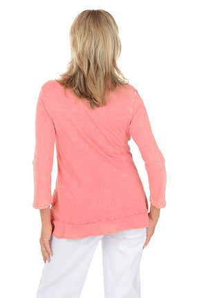 Woman wearing a pink floral blouse with white pants on a white background. Back shot.