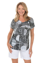 A woman wears a printed grey and white t-shirt and white shorts against a white background.