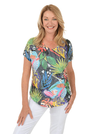 A woman wears a brightly colored t-shirt and white pants against a white background.