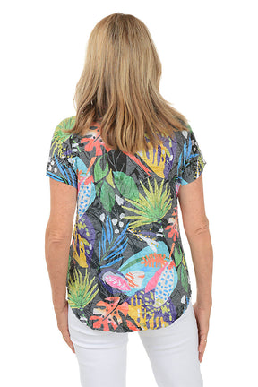 A woman wears a brightly colored t-shirt and white pants against a white background. Back shot.