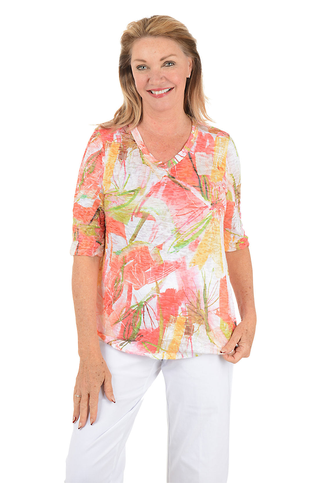 Woman wearing a colorful floral blouse and white pants on a white background.