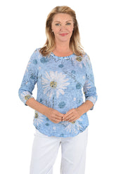 Woman wearing a blue floral blouse with white pants on a white background.