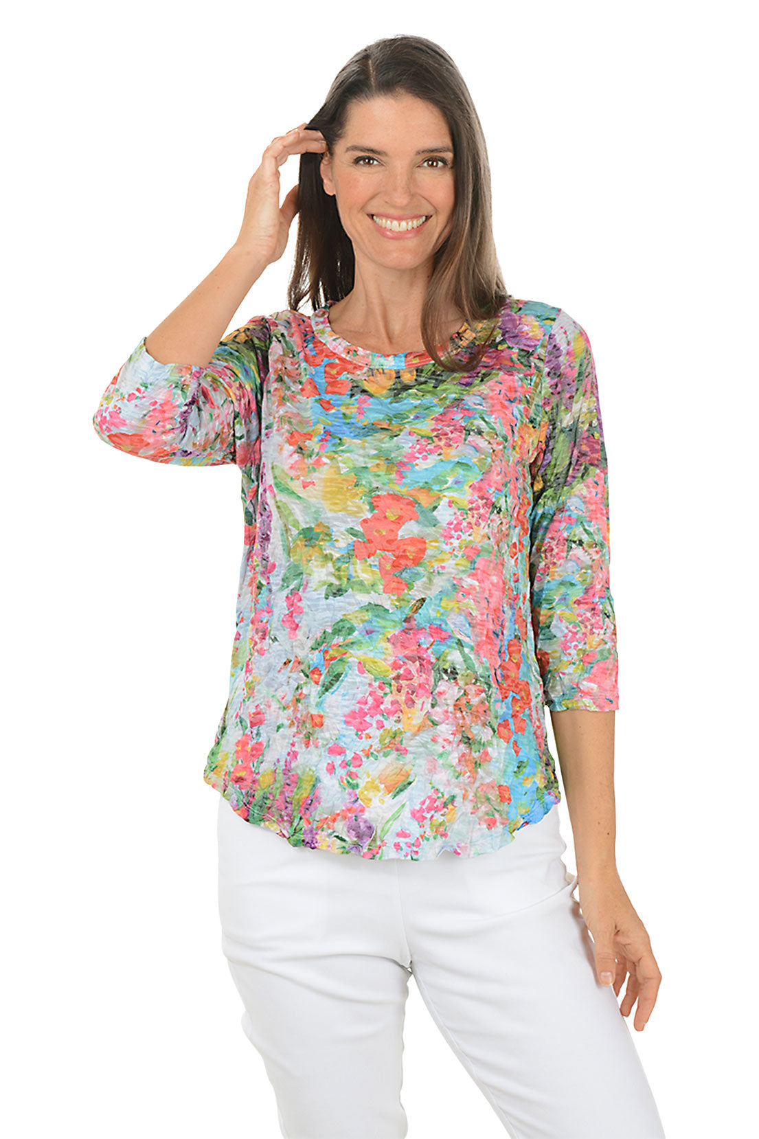 Woman wearing a colorful floral blouse and white pants on a white background.
