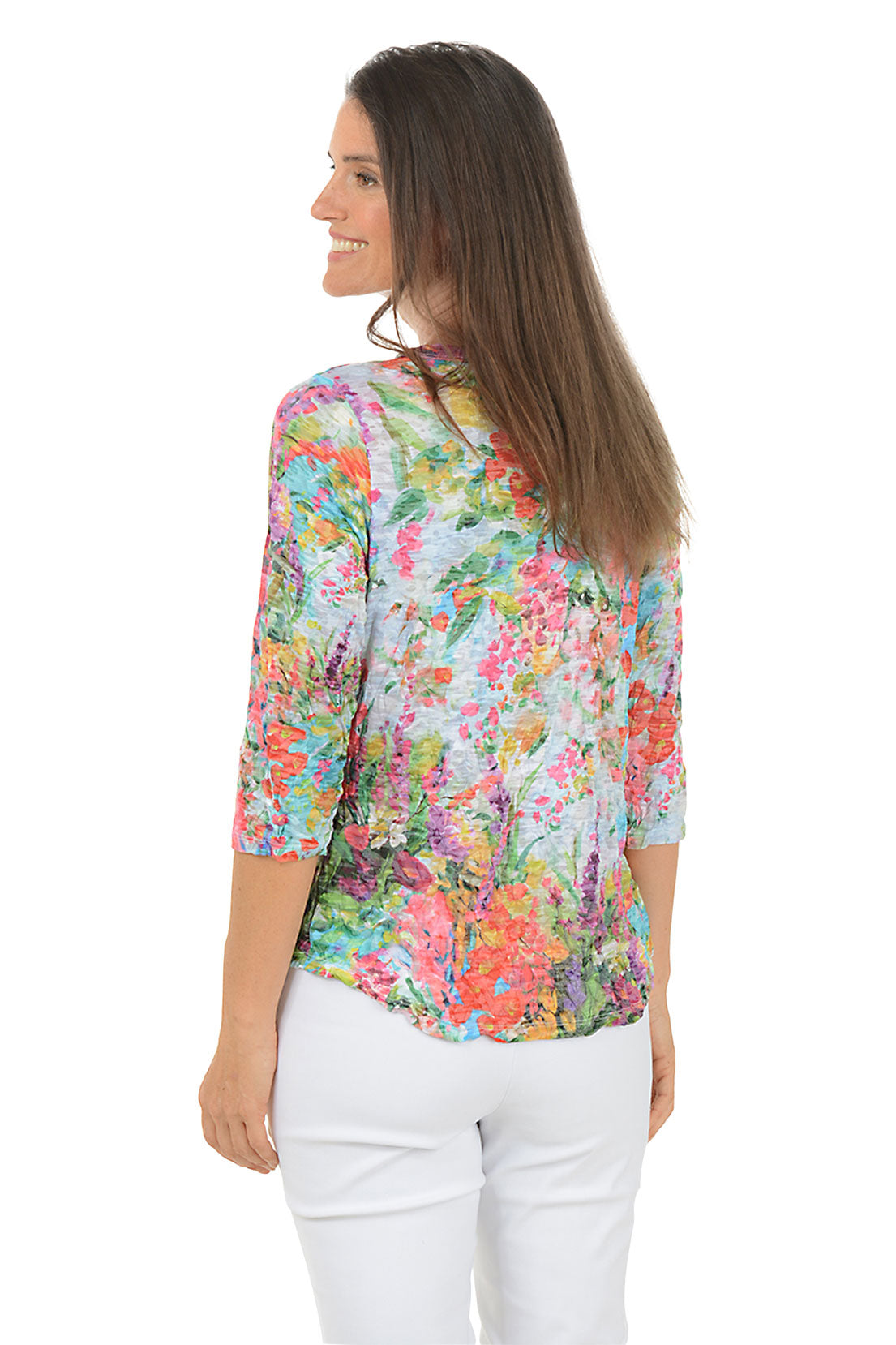 Woman wearing a colorful floral blouse and white pants on a white background. Back shot.