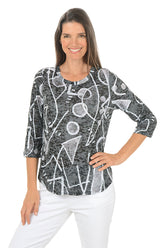 Woman wearing a black and white patterned top with white pants on a white background.