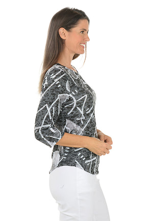 Woman wearing a black and white patterned top with white pants on a white background. Side shot.