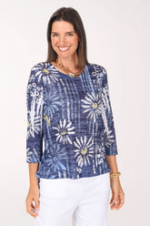 Model wearing the Jess and Jane Upsy Daisy Burnout High-Low Knit Top, white daisies on a navy tie-dye grid, over white pants, front view