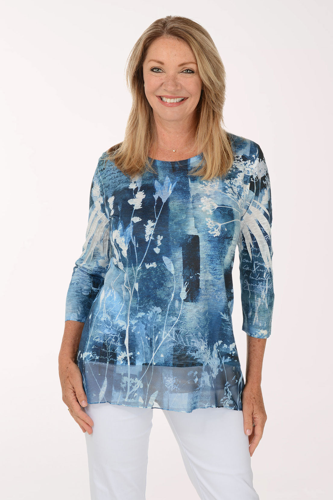 A woman modeling a blue and white abstract patterned long-sleeve tunic top with white pants, photographed against a plain white studio background.