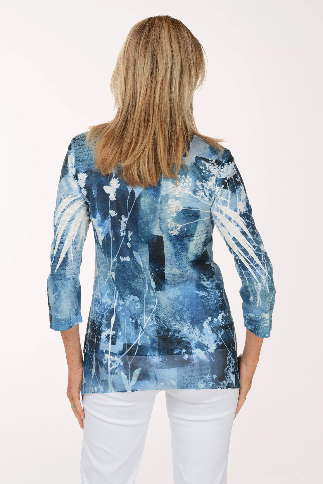 A woman modeling a blue and white abstract patterned long-sleeve tunic top with white pants, photographed against a plain white studio background.