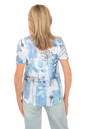 Woman wearing a blue floral patterned shirt on a white background. Back shot.