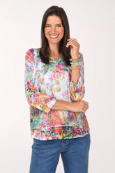Model wearing the Jess and Jane Emilia Mesh Overlay Knit Top, a watercolor floral in pink, coral, green and blue under mesh, with jeans, front view