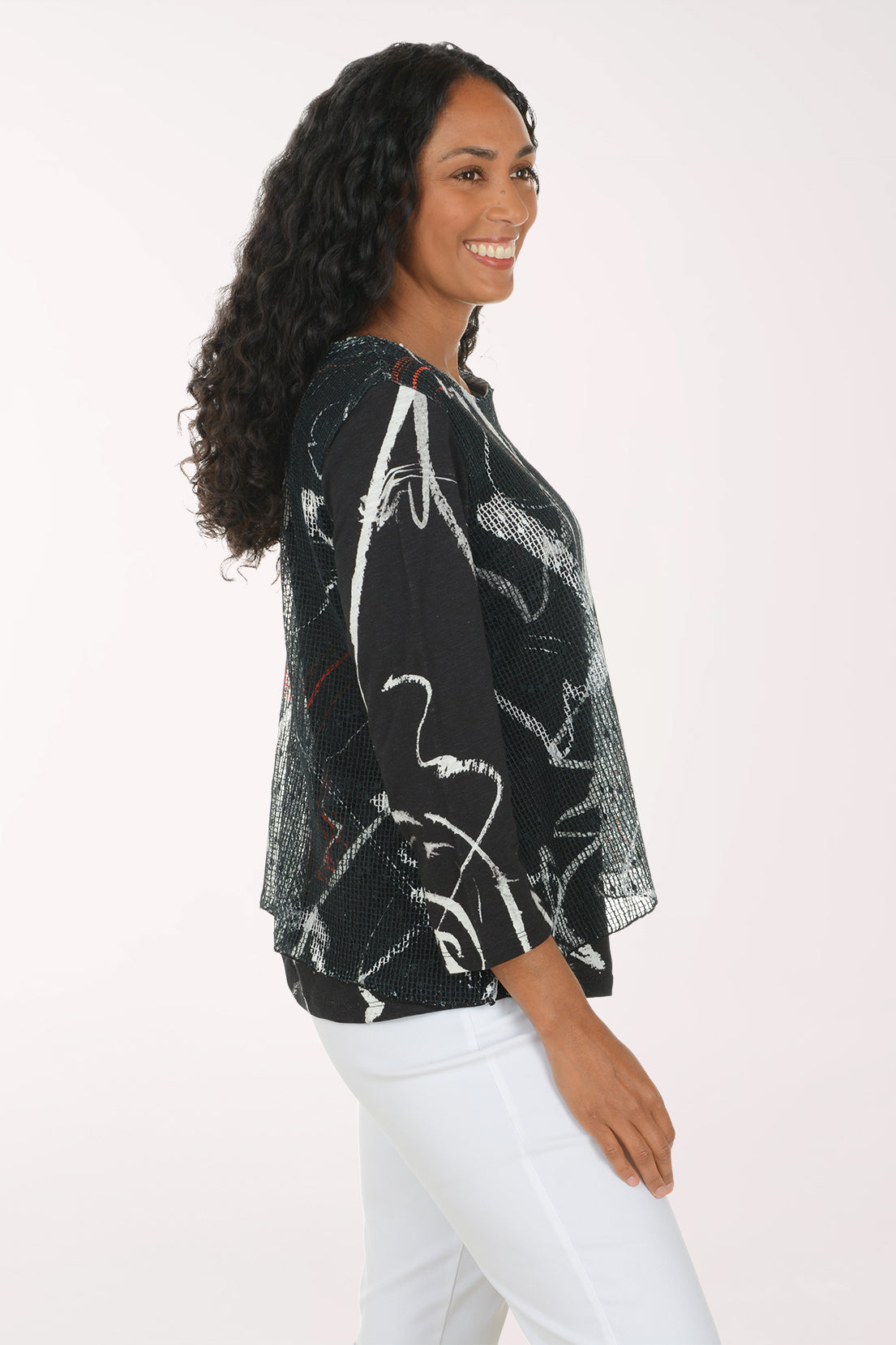 A woman modeling a black long-sleeve top with a white and gray abstract brushstroke pattern and thin red accent lines, paired with white pants, against a plain white studio background.