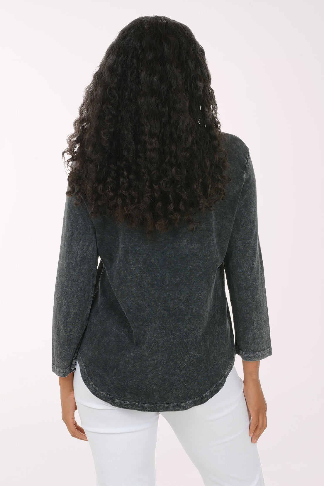A woman viewed from the back wearing a dark charcoal gray mineral-wash long-sleeve top and white pants, set against a plain white studio background.