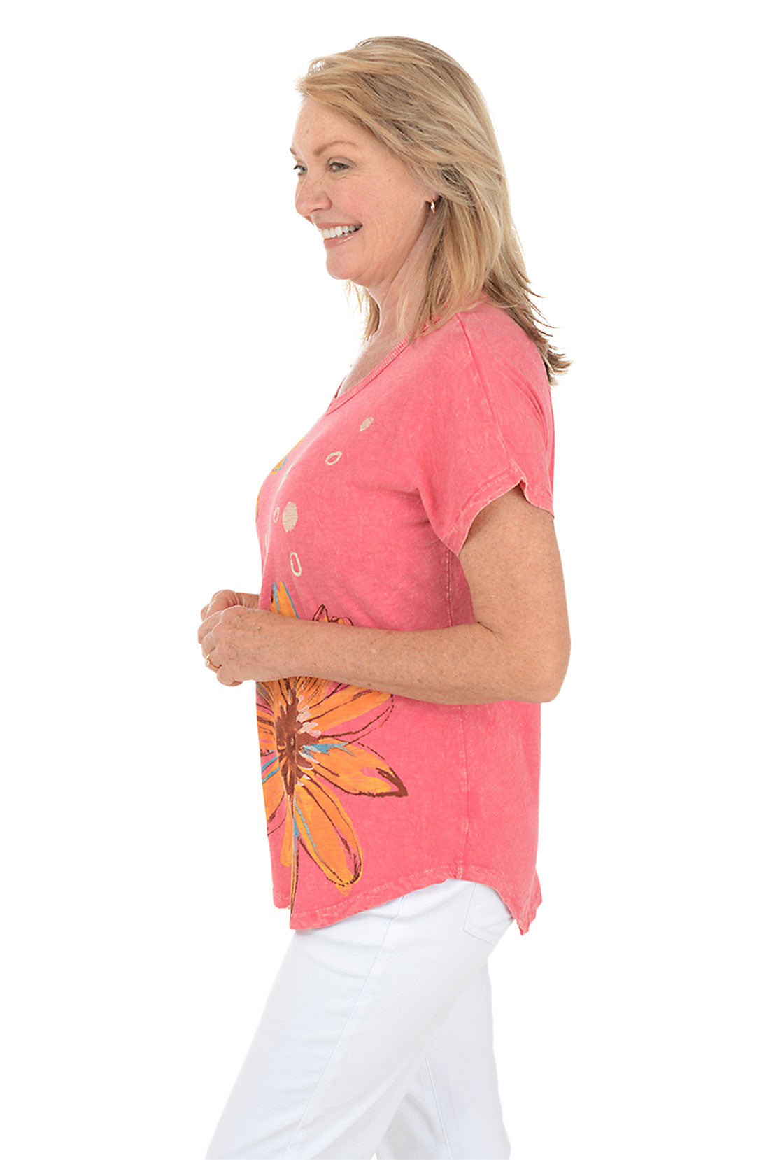Woman wearing a pink t-shirt with orange floral designs on a white background. Side shot.
