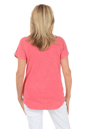 Woman wearing a pink t-shirt with orange floral designs on a white background. Back shot.