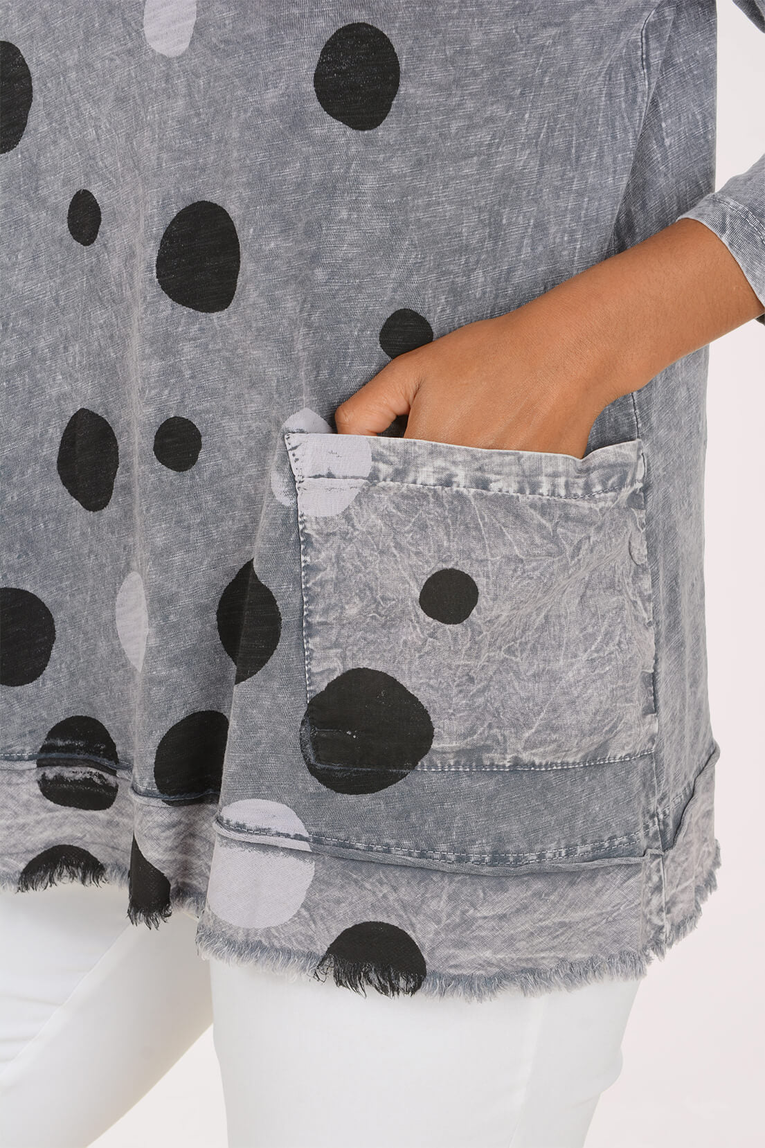 Close-up of a gray mineral-wash tunic top with black and white polka dots, featuring a large front patch pocket and frayed hem, shown on a model.