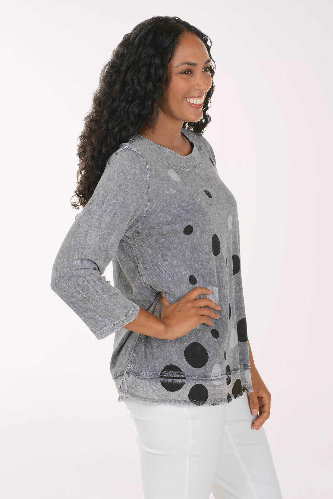 A woman modeling a heather gray long-sleeve top with black and white polka dots, paired with white pants, against a plain white studio background.