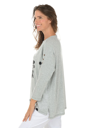 Woman wearing a gray sweater with a floral design on a white background. Side shot.