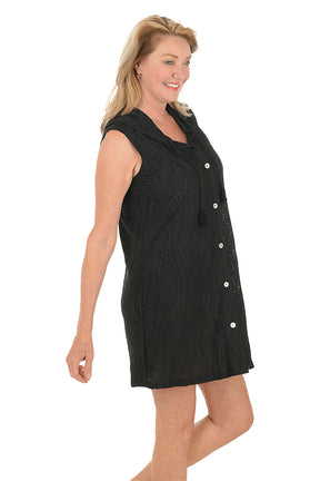 Woman wearing a black sleeveless dress with buttons on a white background. Side shot.