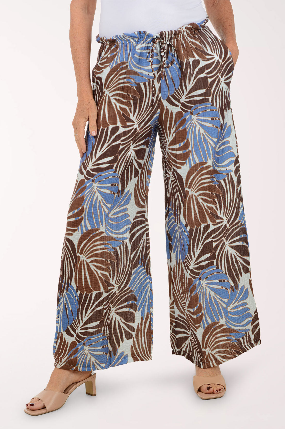 Tropical leaf patterned pants worn by a person on a white background