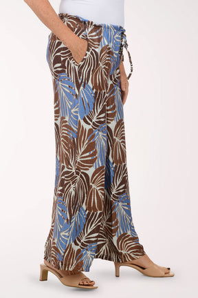 Tropical leaf patterned pants worn by a person on a white background