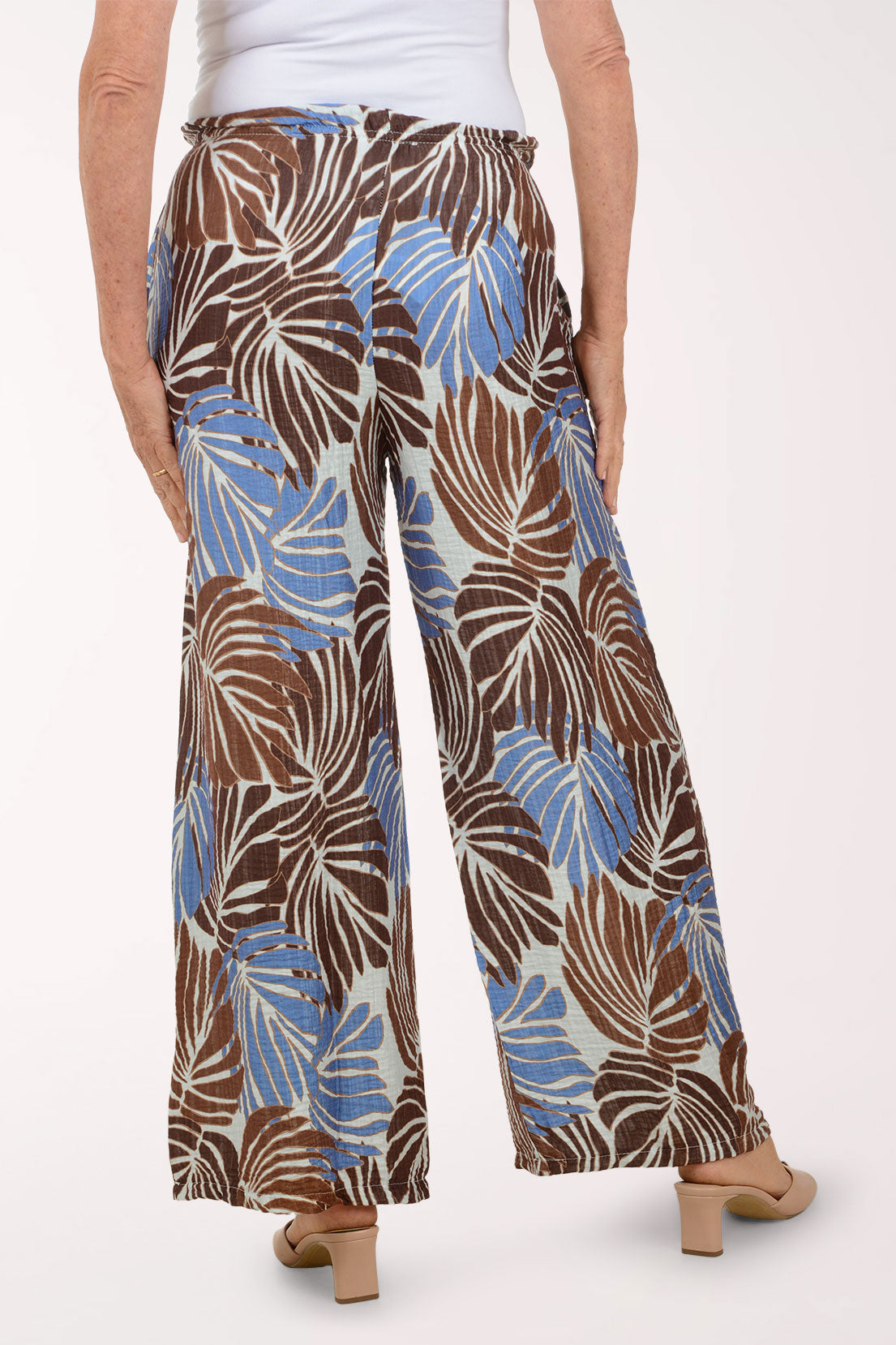 Tropical leaf patterned pants worn by a person on a white background