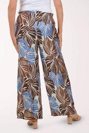 Tropical leaf patterned pants worn by a person on a white background