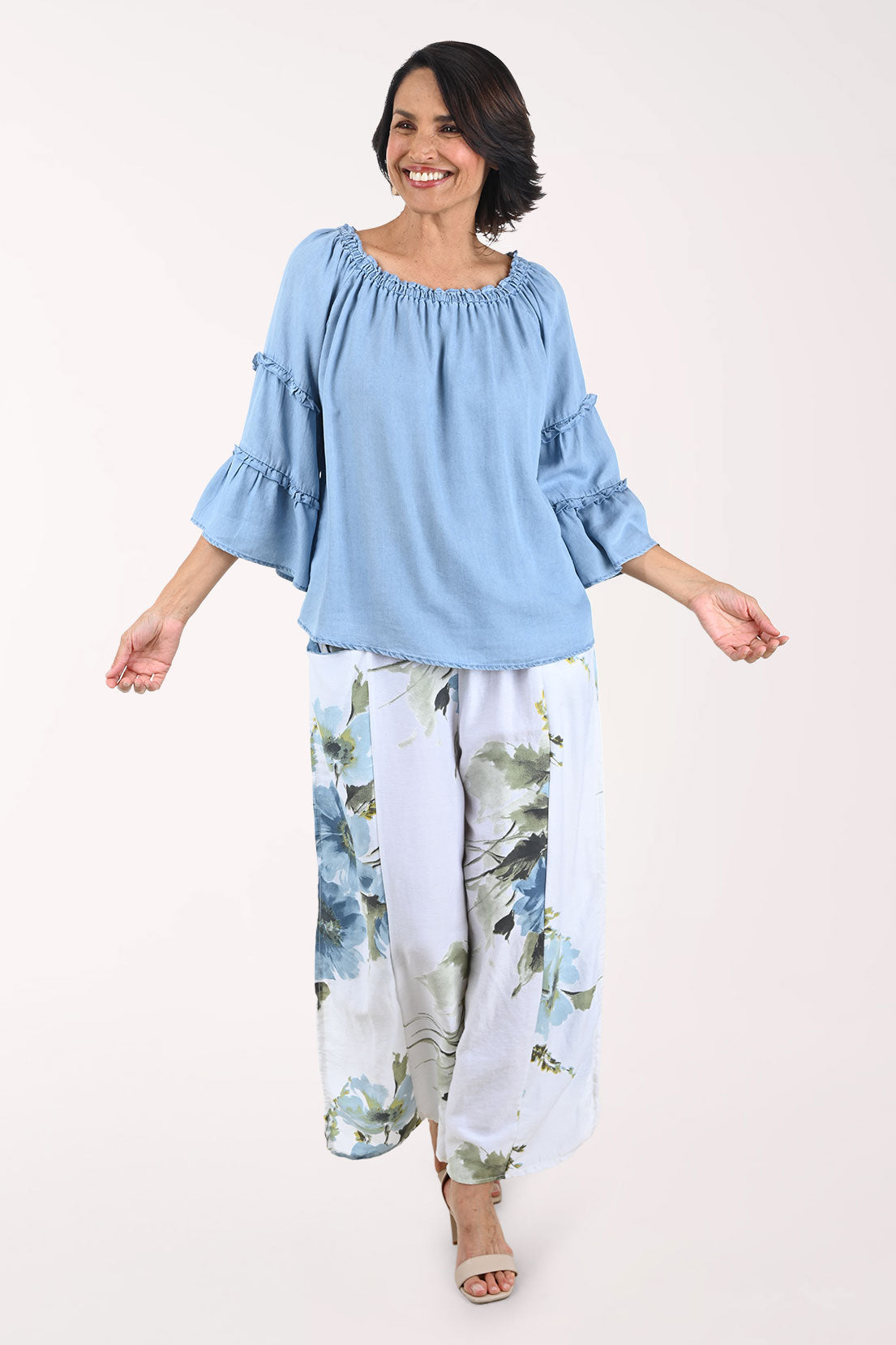 Woman wearing a light blue top and floral pants on a white background