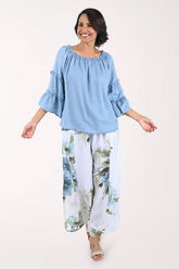 Woman wearing a light blue top and floral pants on a white background