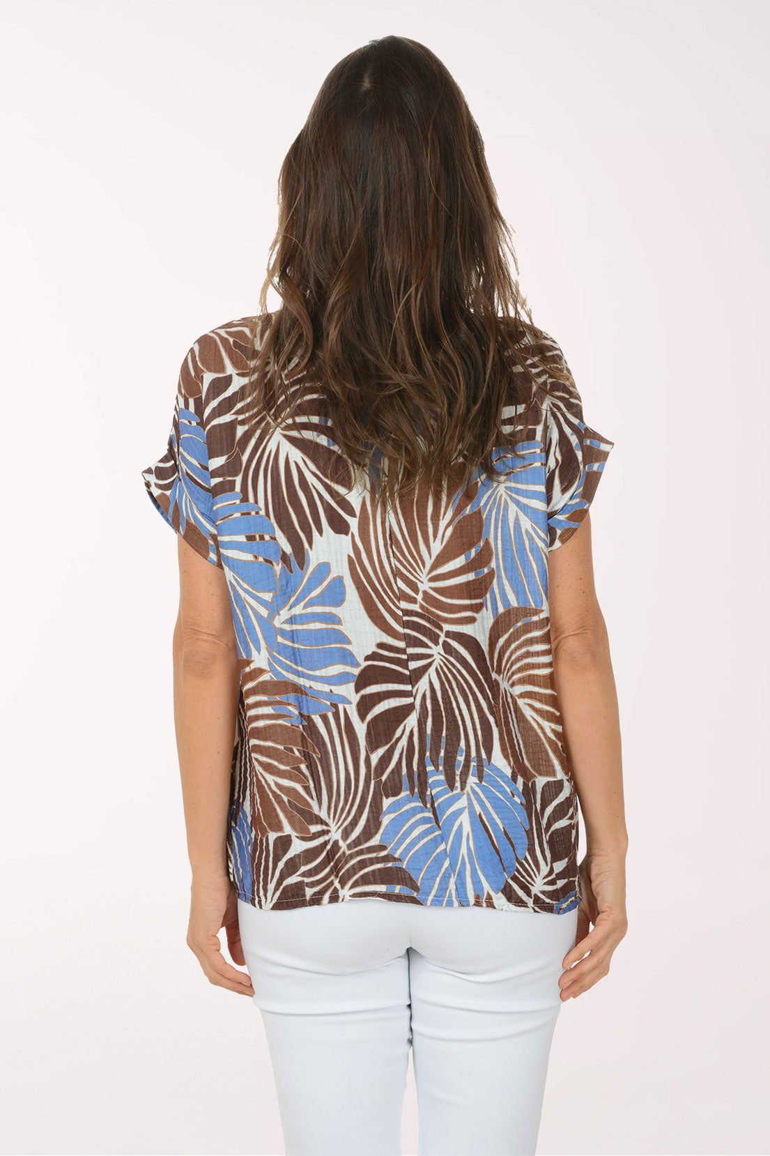 Woman wearing a patterned top with brown, blue, and beige leaves on a white background