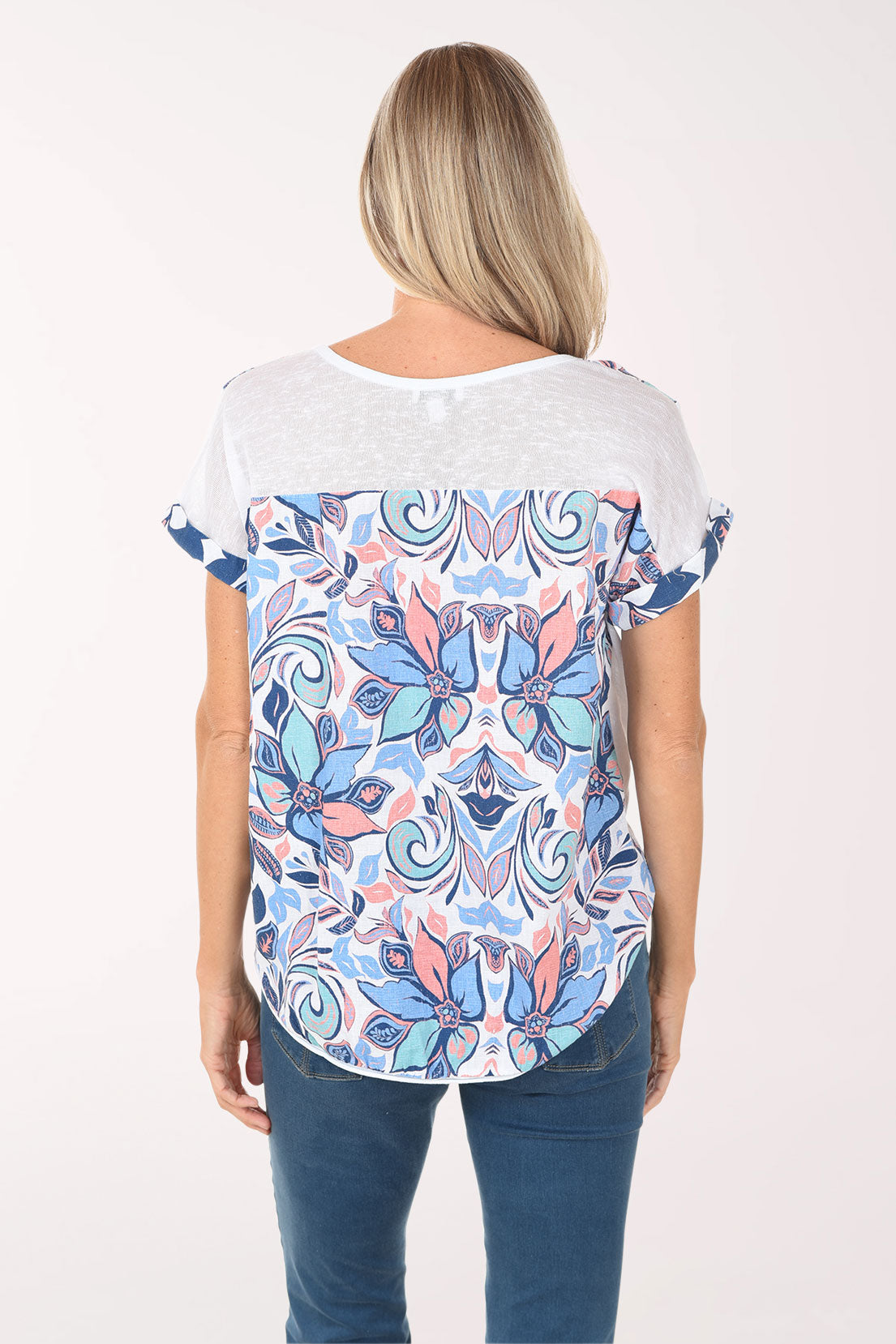 Woman wearing a colorful patterned top and blue jeans on a white background