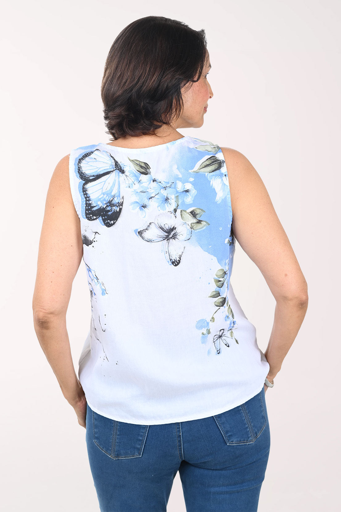 Woman wearing a sleeveless top with butterfly design and blue jeans on a white background