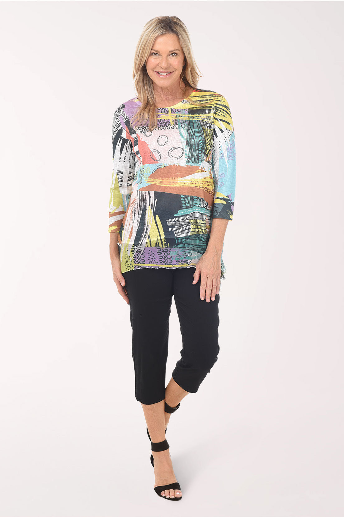 Woman wearing a colorful abstract print top and black pants on a white background